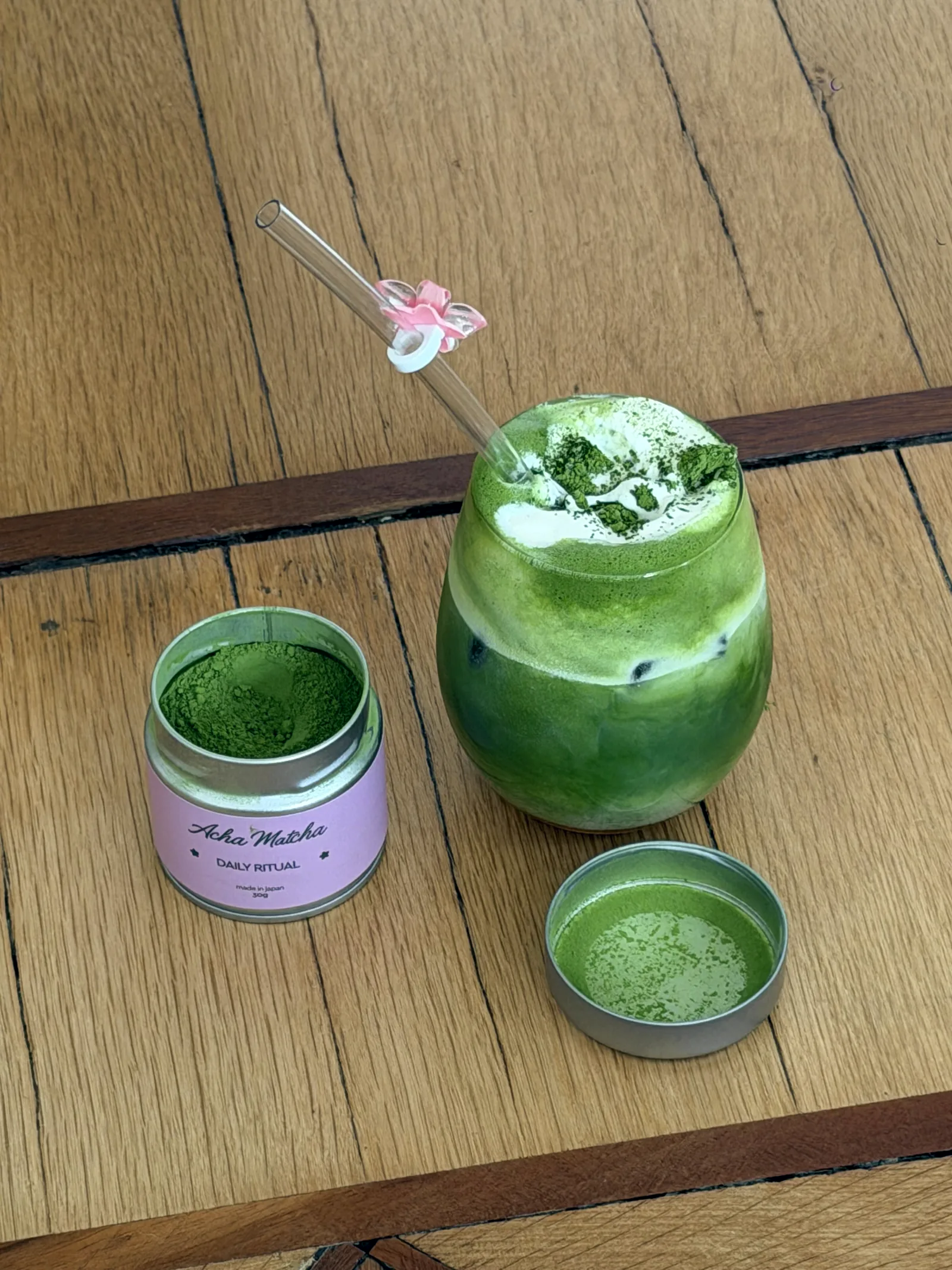 An open tin of matcha powder beside a freshly whisked glass